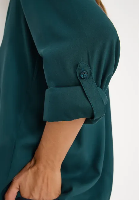 Person mit türkisblauer Bluse, Ärmel hochgekrempelt und geknöpft.